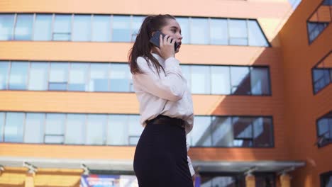 Business-girl-talking-on-the-phone-while-standing-near-the-business-center.-4K