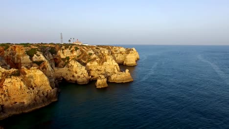 Faro-de-Ponta-da-Piedade-en-acantilado-junto-al-mar-en-vista-aérea-de-la-puesta-del-sol,-Lagos,