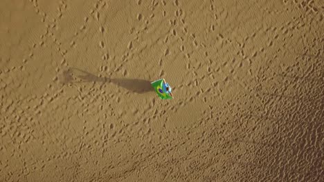 Woman-on-the-sand-with-Brazilian-flag,-aerial-shot