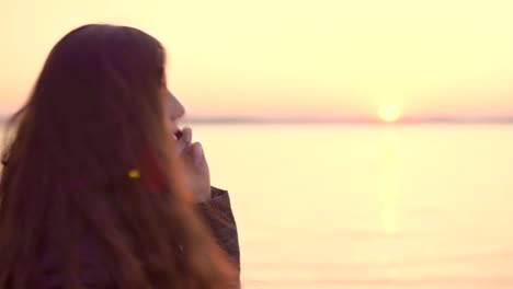 Young-attractive-woman-talking-on-mobile-phone-on-sunset-background-on-lake.-4k