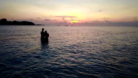 v04148-vuelo-drone-vista-aérea-de-Maldivas-playa-2-personas-pareja-hombre-mujer-amor-romántico-puesta-de-sol-salida-del-sol-en-la-isla-de-paraíso-tropical-soleado-con-cielo-azul-aqua-agua-mar-4k