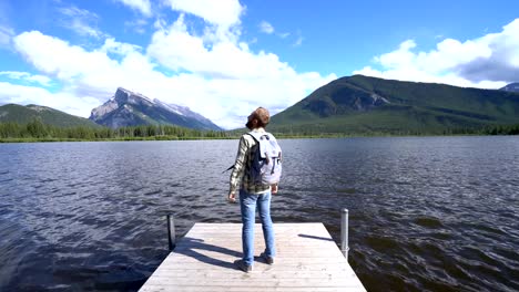 Hombre-de-pie-en-el-muelle-de-madera-en-el-lago-contemplando-la-naturaleza,-impresionantes-paisajes-de-montañas-rocosas-de-Canadá