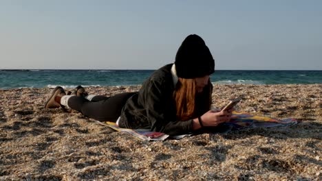 Chica-está-descansando-acostado-en-la-orilla-del-mar-Mediterráneo-en-un-día-frío-de-otoño