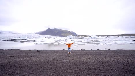 Young-woman-arms-outstretched-at-glacier-lagoon-in-Iceland