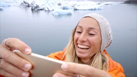 Retrato-de-selfie-de-vídeo-lenta-de-mujer-joven-de-pie-junto-a-la-laguna-glaciar-en-Islandia