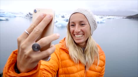 Retrato-de-selfie-de-vídeo-lenta-de-mujer-joven-de-pie-junto-a-la-laguna-glaciar-en-Islandia