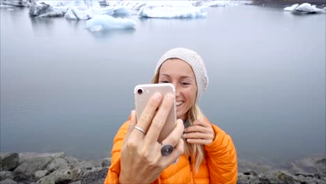 Retrato-de-selfie-de-vídeo-lenta-de-mujer-joven-de-pie-junto-a-la-laguna-glaciar-en-Islandia