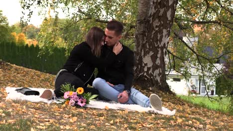 A-young-couple-sits-on-a-white-bedspread-in-autumn-park