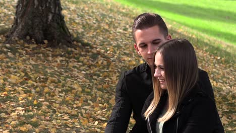 A-young-couple-sits-on-a-white-bedspread-in-autumn-park