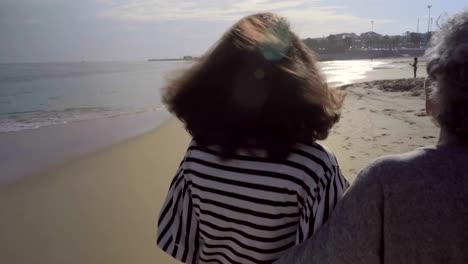 Two-smiling-women-hugging-and-walking-on-tropical-beach.