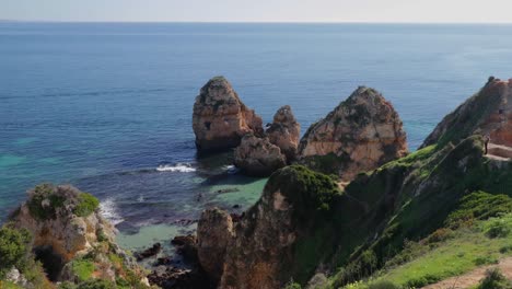 Ponta-da-Piedade,-lugar-famoso-en-el-sur-de-Portugal,-la-ciudad-de-lagos,-la-costa-rocosa,-olas-de-océano-Atlántico,-rocas-afiladas,-agua-azul,-flores-amarillas,-arco,-nadie,-playa-salvaje