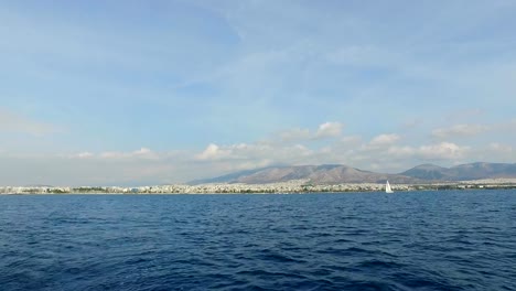 Se-puede-ver-el-paisaje-de-las-montañas-y-el-mar-Mediterráneo,-en-la-distancia-usted-puede-ver-las-casas-de-Atenas,-Grecia.-Verano-claro-día,-nubes-blancas-en-el-cielo,-el-mar-en-calma.-Vista-desde-el-mar