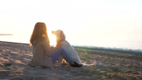 Hembra-joven-rápida-jugando-con-perro-retriever-en-la-playa-al-atardecer