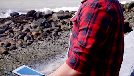 Man-in-headphones-using-digital-tablet-at-seaside-4k