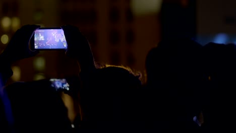 Spectator-man-recording-video-with-zoom-of-stage-and-big-screen-via-smartphone-at-outdoor-music-concert