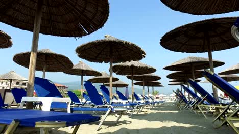 Walk-on-sand-beach-among-umbrellas-and-lounge-beds.-Vacation-at-sea,-beautiful-beach-and-straw-umbrellas-under-blue-sky,-4k-steadicam-shot