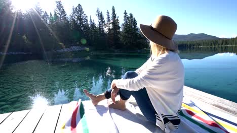 Mujer-sentada-en-el-muelle-de-madera-por-el-impresionante-lago-alpino-contemplando-la-naturaleza