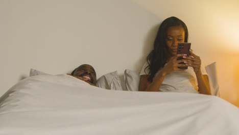 Couple-At-Home-At-Night-Lying-In-Bed-With-Woman-Looking-At-Mobile-Phone-3