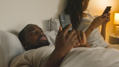 Couple-With-Relationship-Problems-At-Home-At-Night-Lying-In-Bed-Both-Looking-At-Mobile-Phones-1