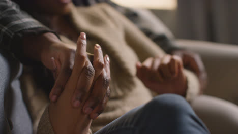 Close-Up-Of-Loving-Couple-Holding-Hands-Relaxing-At-Home-Sitting-On-Sofa-Talking-Together