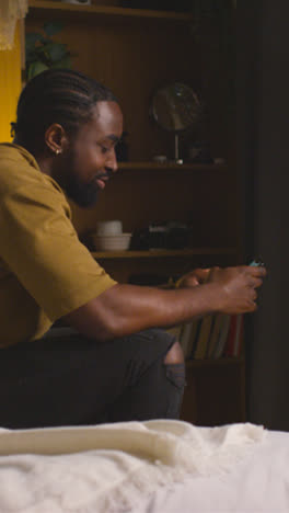 Vertical-Video-Of-Young-Man-Relaxing-At-Home-At-Night-In-Bedroom-Looking-At-Mobile-Phone-1