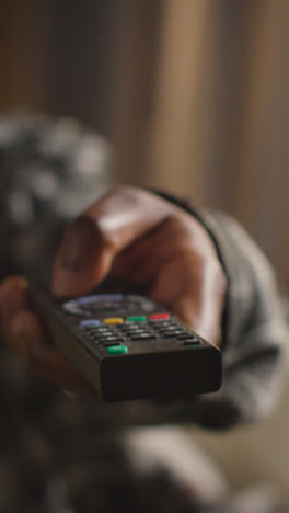 Vertical-Video-Close-Up-Of-Man-Relaxing-At-Home-Sitting-On-Sofa-Changing-TV-Channels-With-Remote-Control