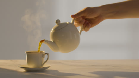 Studioaufnahme-Einer-Person,-Die-Mithilfe-Einer-Teekanne-Eine-Traditionelle-Britische-Tasse-Tee-Zubereitet-Und-Einschenkt