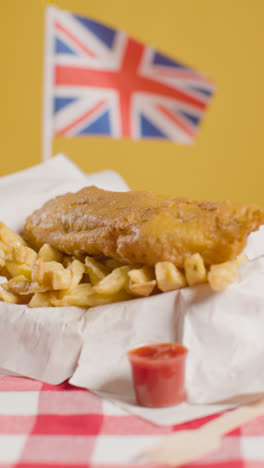 Vertical-Video-Of-Traditional-British-Takeaway-Meal-Of-Fish-And-Chips-With-Union-Jack-Flag-2