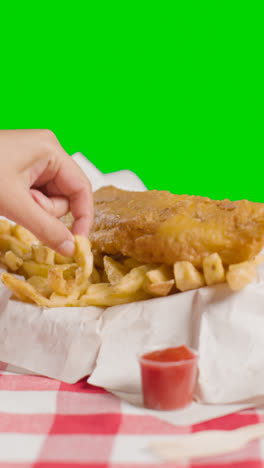 Vertikales-Video-Von-Menschen,-Die-Mit-Den-Fingern-Traditionelle-Britische-Gerichte-Zum-Mitnehmen-Mit-Fisch-Und-Chips-Auf-Grünem-Hintergrund-Essen