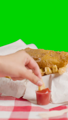 Vertical-Video-Of-People-Using-Fingers-To-Eat-Traditional-British-Takeaway-Meal-Of-Fish-And-Chips-With-Ketchup-On-Green-Screen