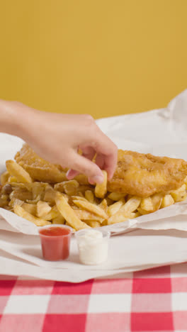 Vertikales-Video-Von-Menschen,-Die-Mit-Den-Fingern-Ein-Traditionelles-Britisches-Imbissgericht-Mit-Fish-And-Chips-Mit-Ketchup-Und-Mayo-Essen