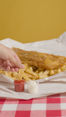 Vertical-Video-Of-People-Using-Fingers-To-Eat-Traditional-British-Takeaway-Meal-Of-Fish-And-Chips-With-Ketchup-and-Mayo-1