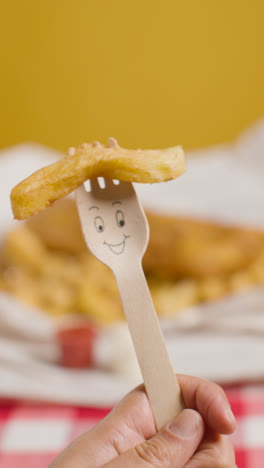 Vertical-Video-Of-Person-Eating-Traditional-British-Takeaway-Meal-Of-Fish-And-Chips-Holding-Wooden-Fork-With-Smiling-Face