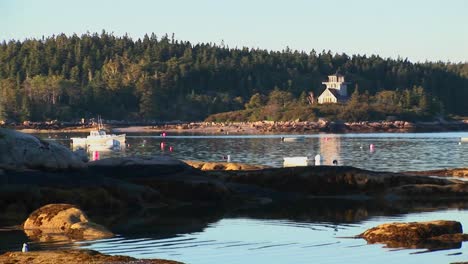 An-anchored-boat-floats-near-a-lobster-village-with-a-tree-covered-mountain-in-Stonington-Maine-