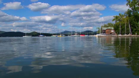 A-cloudy-blue-sky-and-sailboats-are-seen-in-the-distance-of-a-glassy-rural-lake-in-Central-Vermont--