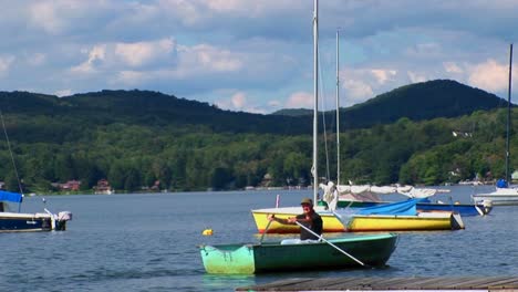 A-man-drifts-in-a-rowboat-near-sailboats-and-a-dock-on-a-rural-lake-in-Central-Vermont-
