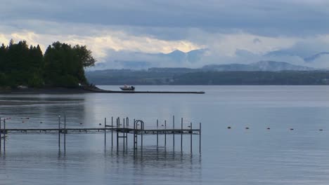 A-small-dock-extends-into-calm-waters-below-a-grey-and-cloudy-sky-at-Lake-Champlain-in-Vermont
