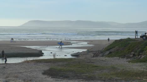 A-surfer-walks-across-an-estuary-along-the-Central-California-coast