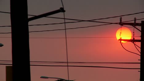 A-orange-ball-of-sun-sets-behind-power-lines-during-fire-season-in-California