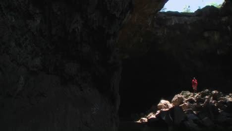 Hermosa-Sartén-A-Través-De-Una-Cueva-Oscura-Y-Profunda-Para-Revelar-A-Un-Guerrero-Masai-De-Pie-En-Un-Charco-De-Luz-En-Kenia