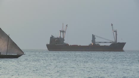 A-dhow-sailboat-sails-bast-a-modern-freighter-cargo-ship-off-the-coast-of-Zanzibar