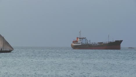Ein-Dhau-Segelboot-Fährt-An-Einem-Modernen-Frachtschiff-Vor-Der-Küste-Von-Sansibar-Vorbei