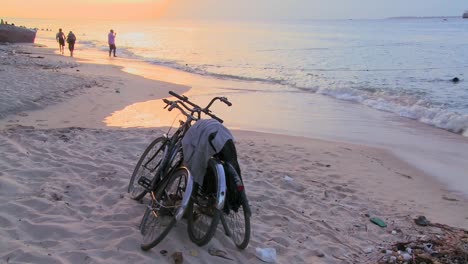 Sunset-shot-along-a-beach-with-two-bicycles-parked-on-the-shore-and-niños-playing-in-distance