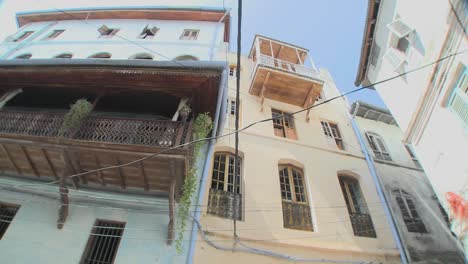 A-low-angle-shot-looking-directly-up-at-tall-old-buildings-lining-the-narrow-alleys-of-Stone-Town-Zanzibar