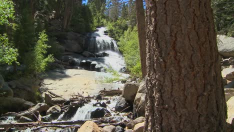 A-moving-shot-past-a-tree-to-reveal-a-beautiful-alpine-waterfall