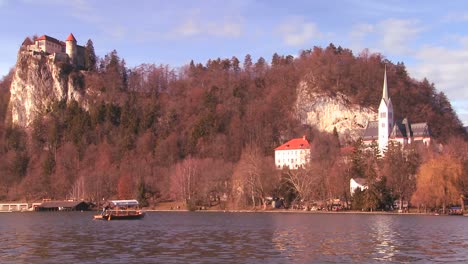 Ein-Boot-Fährt-An-Einer-Wunderschönen-Mittelalterlichen-Burg-Und-Kirche-Am-Ufer-Des-Sees-Von-Bled-Slowenien-Vorbei-1