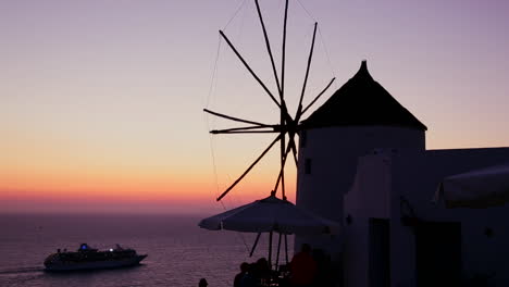 Ein-Kreuzfahrtschiff-Fährt-In-Der-Dämmerung-Oder-Bei-Sonnenuntergang-An-Windmühlen-Auf-Der-Romantischen-Griechischen-Insel-Santorini-In-Der-Dämmerung-Vorbei-1