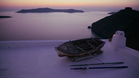 Ein-Ruderboot-Sitzt-Auf-Einem-Dach-Vor-Einem-Wunderschönen-Sonnenuntergang-Hinter-Inseln-Der-Griechischen-Inseln-Behind
