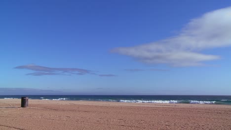 Ein-Leerer-Strand-Mit-Einer-Einsamen-Mülltonne-Und-Blauem-Himmel