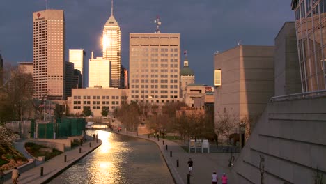 Wide-shot-of-Indianapolis-Indiana-river-walk-at-dusk-with-sun-glinting-off-buildings-1